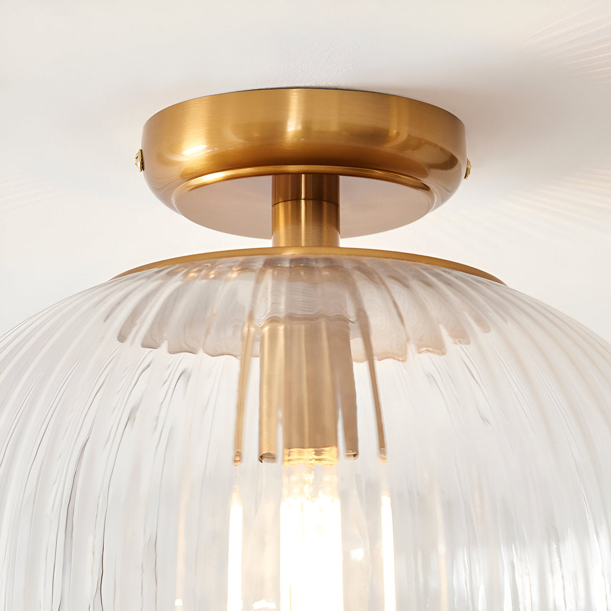 Langton Flush Downlight in brass with a ribbed glass globe shade and single E27 lamp, close-up view against a plain white ceiling.