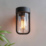 Caldwell Wall Light in matt black die-cast aluminium with clear glass shade and visible E27 bulb, industrial style, shown lit against a plain wall.