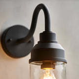 Close-up of the Endon Cranworth wall light in matt black die-cast aluminium, showing the curved arm, round backplate and clear glass shade with E27 bulb.