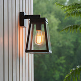 Caldwick Wall Light in matt black, a lantern-style fixture with clear glass panels and exposed bulb, mounted on exterior wall cladding.