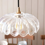 Ashwick clear glass pendant shade with scalloped edge and brass fitting, shown close-up with visible bulb, in a room with wooden chairs.