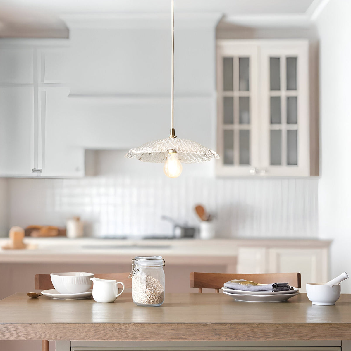 Endon Castshaw pendant light with rippled clear glass shade and brass fitting on braided flex, hanging above a wooden dining table in a white kitchen.