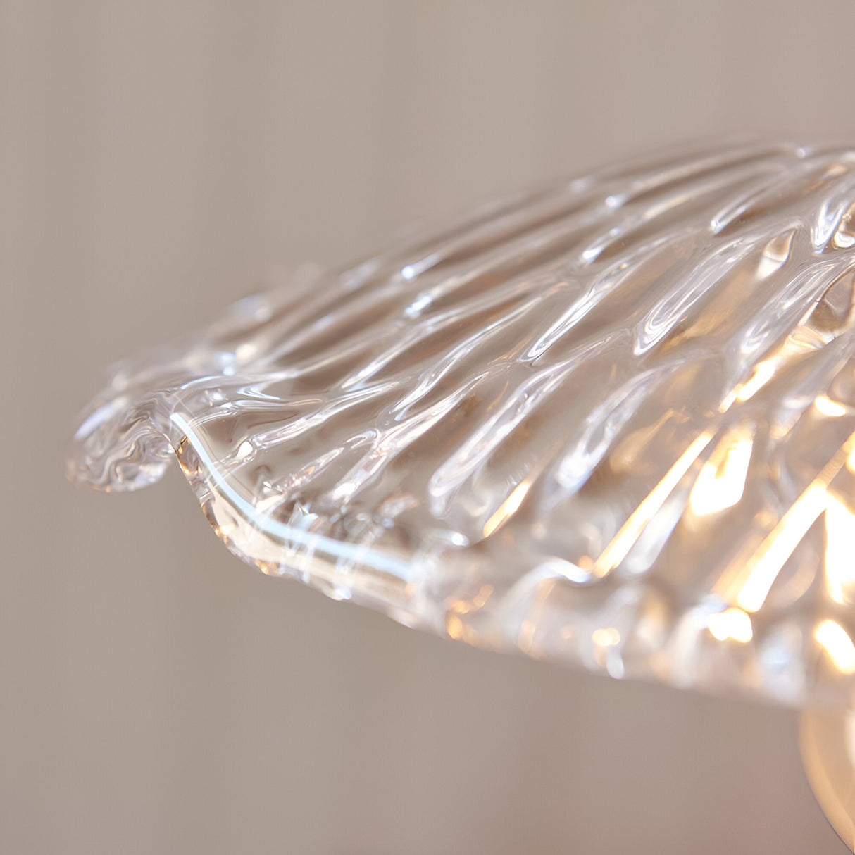 Close-up of the Endon Castshaw pendant shade edge showing heavy clear glass with a rippled, shell-like texture catching warm light on a neutral background.