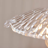 Close-up of the Endon Castshaw pendant shade edge showing heavy clear glass with a rippled, shell-like texture catching warm light on a neutral background.