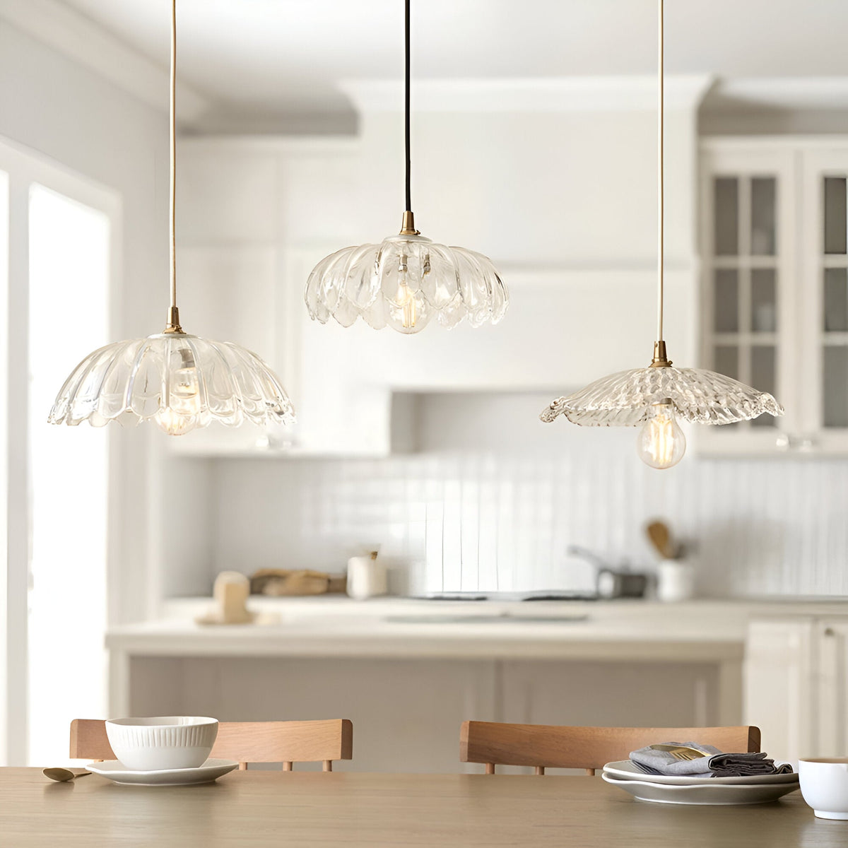 Three Endon Castshaw clear rippled glass pendant shades with brass fittings hanging at varied heights over a dining table in a bright white kitchen.