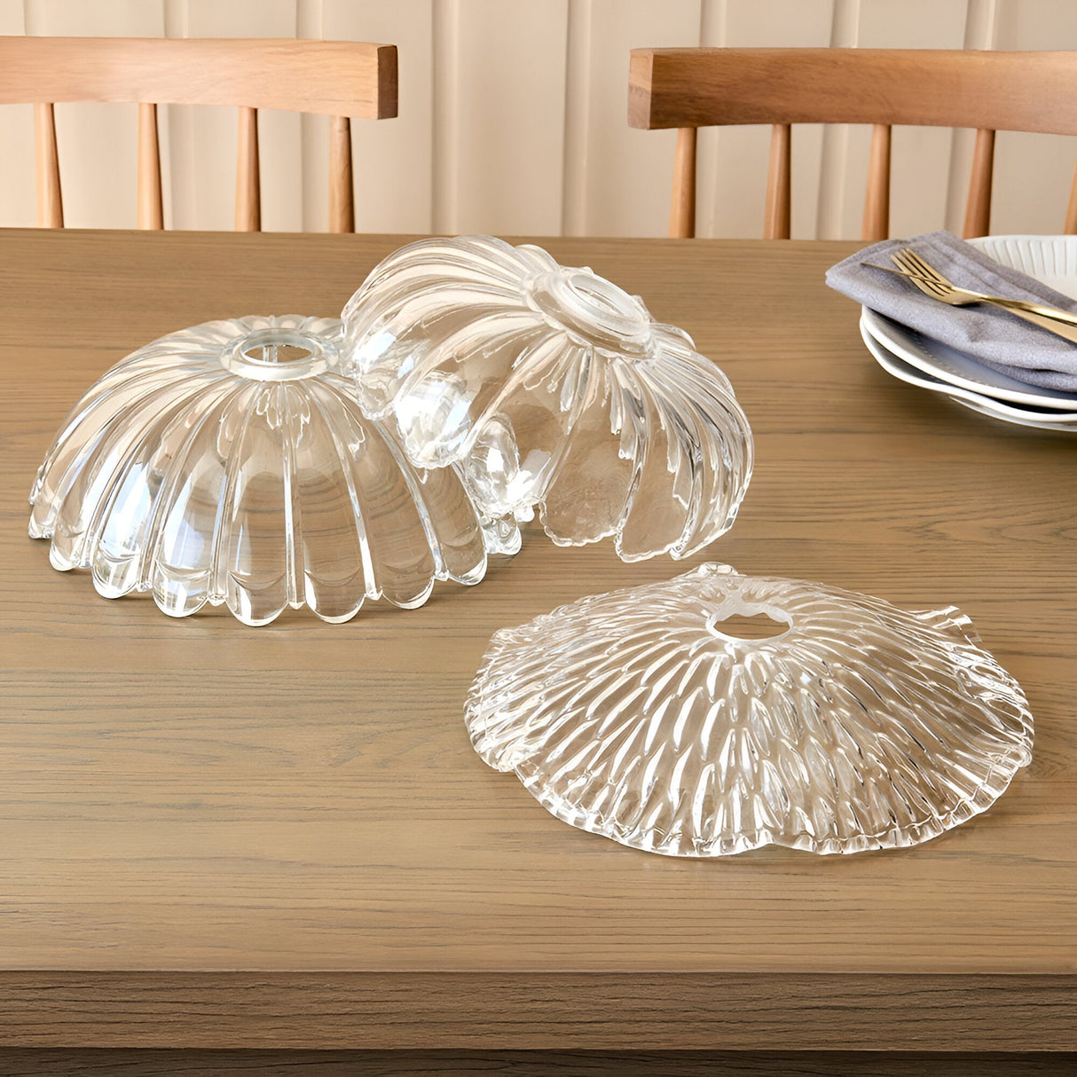 Three Endon Castshaw clear glass easyfit pendant shades with rippled, shell-like textures displayed on a wooden dining table beside plates and cutlery.
