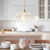 Endon Bevcombe clear glass pendant shade with scalloped domed form and brass fitting, hung above a kitchen island and dining table setting.