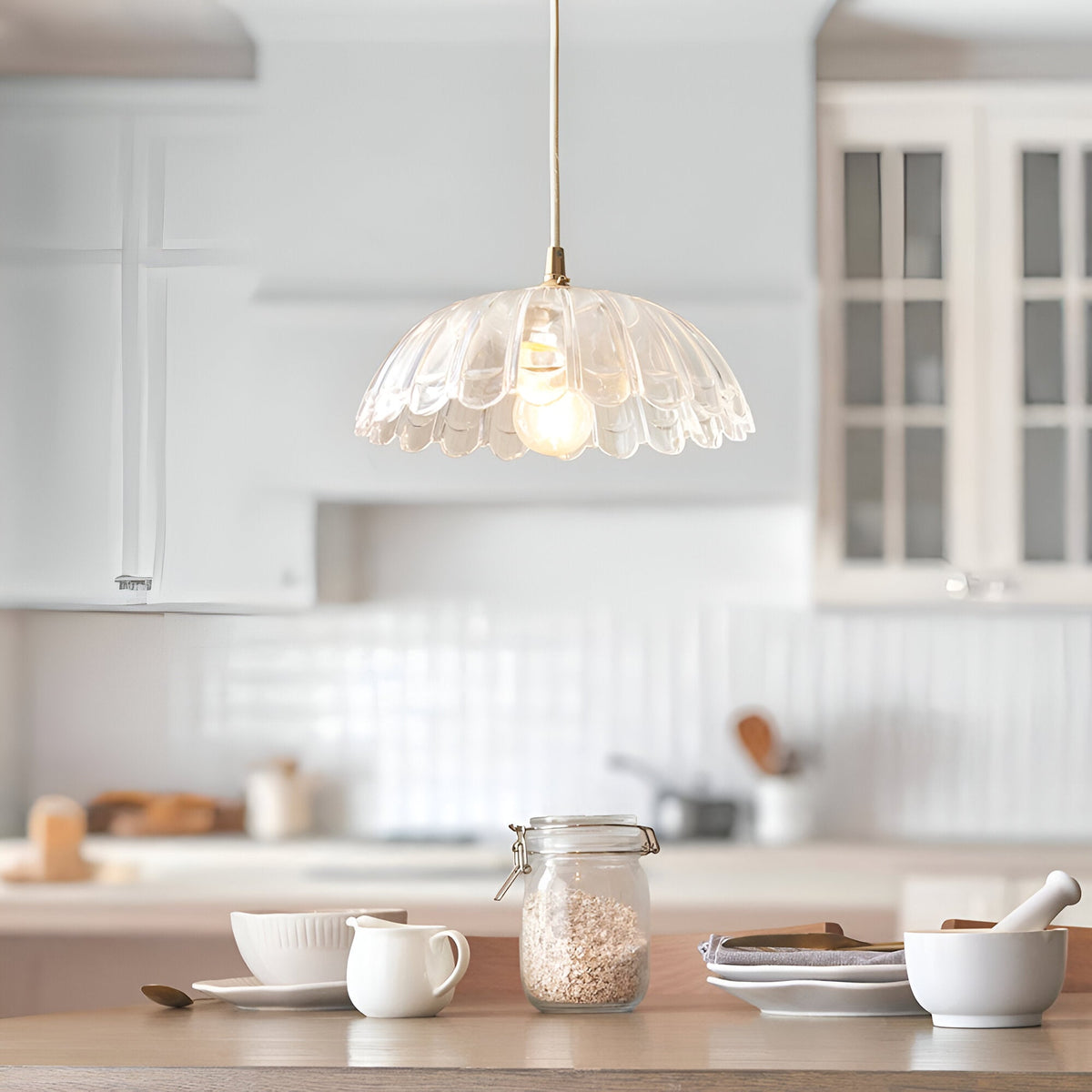Endon Bevcombe clear glass pendant shade with scalloped domed form and lit filament bulb, hanging above a wooden kitchen worktop with ceramics.