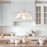 Endon Bevcombe clear glass pendant shade with scalloped domed form and lit filament bulb, hanging above a wooden kitchen worktop with ceramics.