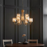 Clementine 9 Light Tiered Chandelier in antique brass with faceted crystal glass shades, hung above a dining table against dark panelled walls.