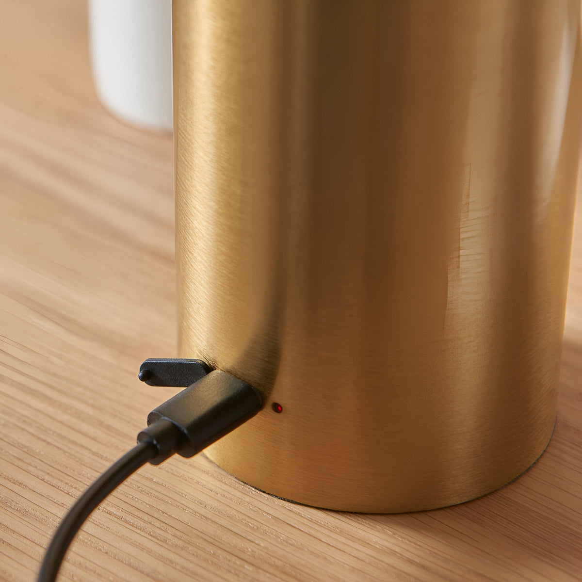 Close-up of the Cranbourne LED Table Lamp in brushed brass, showing the USB charging port and indicator light at the base on a wooden surface.