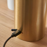 Close-up of the Cranbourne LED Table Lamp in brushed brass, showing the USB charging port and indicator light at the base on a wooden surface.