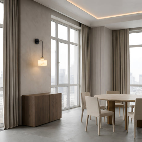 Modern dining room with large windows, beige curtains, a round wooden table and four matching chairs, a wooden sideboard, and the Caelune 1 Light Suspended Stone Alabaster Wall Light in soft white & black. Neutral tones with city views.