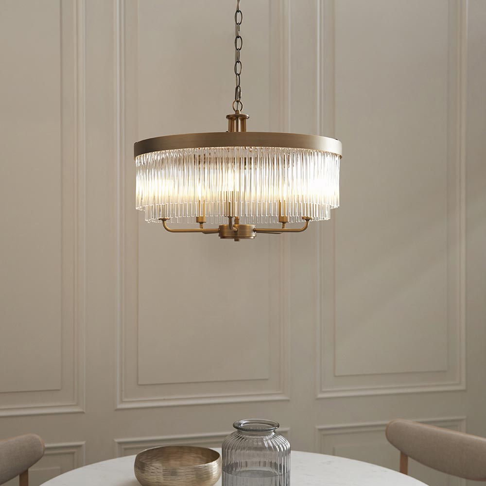 Endon Chatsworth 5 light pendant in antique brass with double tier of clear glass rods, suspended by chain above a dining table against panelled walls.
