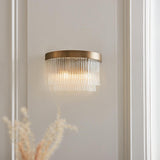 Chatsworth 2 Light Wall Light in antique brass with tiered clear glass rods, illuminated on a hallway wall beside dried florals.