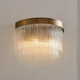 Chatsworth 2 Light Wall Light in antique brass, with curved metal backplate and cascading clear glass rods, mounted on a light wall and softly illuminated.