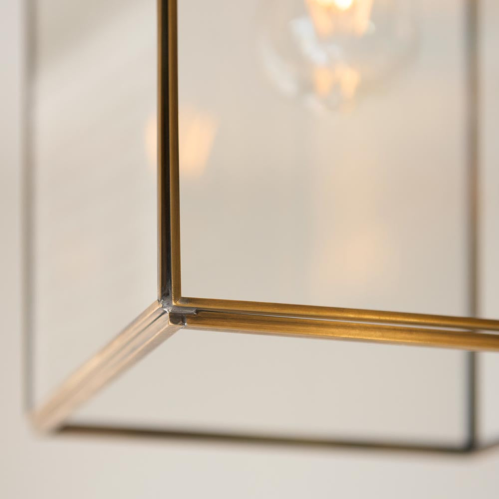 Close-up of the Endon Haddon Grand Pendant corner, showing brushed aged brass framework, clear glass panels, and a warm exposed bulb above.