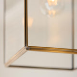 Close-up of the Endon Haddon Grand Pendant corner, showing brushed aged brass framework, clear glass panels, and a warm exposed bulb above.