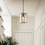 Haddon Pendant in brushed brass, a lantern-shaped fixture with clear glass panels and exposed bulb, hung on chain in a hallway with white doors.