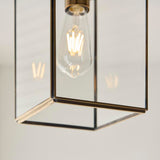Close-up of the Haddon Pendant in brushed brass, showing the lantern-style frame with clear glass panels and an exposed E27 filament bulb.