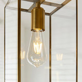 Haddon Pendant in brushed brass, close-up of the lantern frame with clear glass panels around an exposed E27 filament bulb.