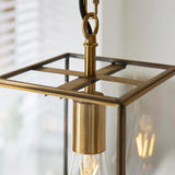 Close-up of the Haddon Pendant in brushed brass, showing the lantern-style frame, clear glass panel, E27 bulb holder, and fabric flex with chain link.