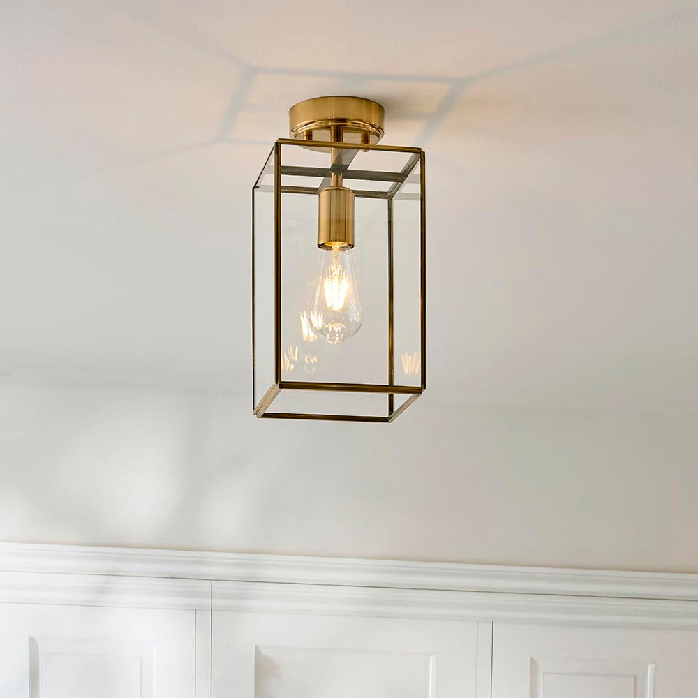 Endon Haddon flush ceiling light in aged brass with a rectangular glass box shade and single E27 bulb, mounted to a white ceiling above panelled walls.