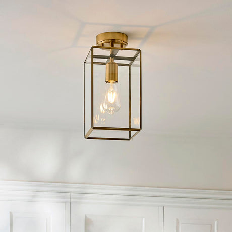 Endon Haddon flush ceiling light in aged brass with a rectangular glass box shade and single E27 bulb, mounted to a white ceiling above panelled walls.