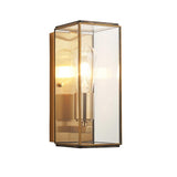 Haddon Wall Light in Antique Brass, a box-lantern design with brushed brass metalwork, clear glass panels, and an exposed filament bulb.