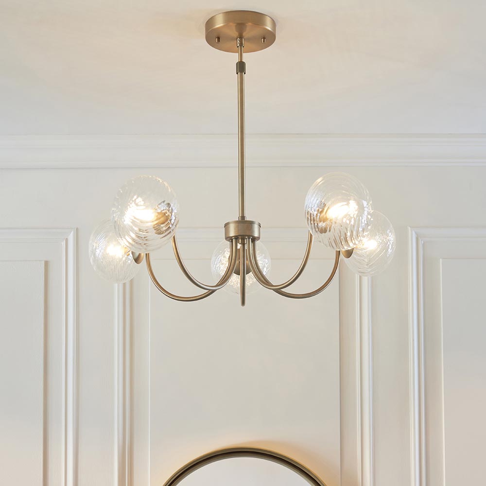 Bramwick 5 Light Pendant in antique brass with curved arms and clear twisted glass shades, shown hanging in a white panelled room.