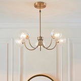 Bramwick 5 Light Pendant in antique brass with curved arms and clear twisted glass shades, shown hanging in a white panelled room.