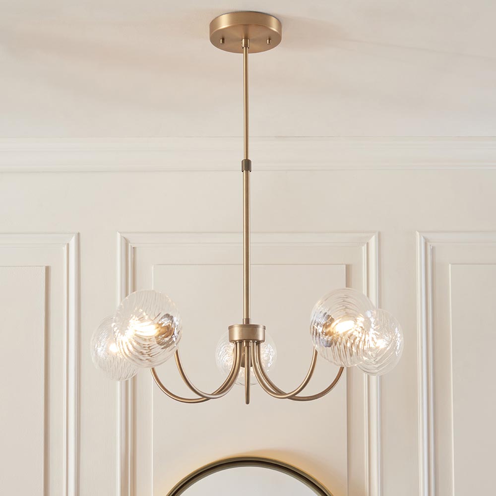 Bramwick 5 Light Pendant in antique brass with curved arms and clear twisted glass shades, hung from a ceiling rose in a panelled room.