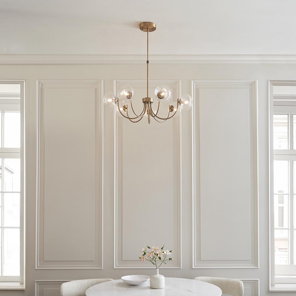 Endon Bramwick 7 light pendant in antique brass with curved arms and clear twisted glass shades, hanging in a panelled dining room between tall windows.