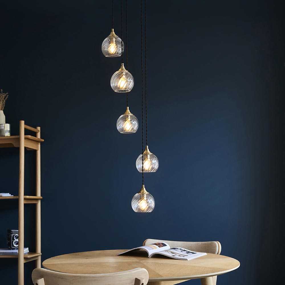 Endon Georgiana 5 light cascade pendant in antique brass with staggered spiral clear glass shades on black cables, above a wooden dining table.
