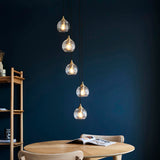 Endon Georgiana 5 light cascade pendant in antique brass with staggered spiral clear glass shades on black cables, above a wooden dining table.
