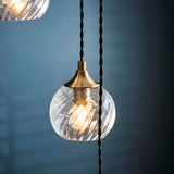 Endon Georgiana cascade pendant shade in antique brass with clear spiral glass globe and black twisted fabric cable, shown against a dark blue background.