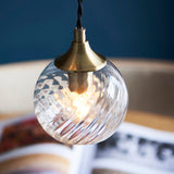 Endon Georgiana pendant light with a single clear spiral glass globe shade and antique brass fitting, suspended from a black cable against a dark blue backdrop.