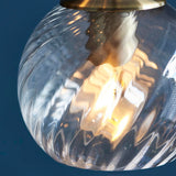 Close-up of an Endon Georgiana cascade pendant globe, showing a clear spiral glass shade with antique brass fitting and lit E14 bulb inside.