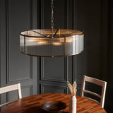 Endon Rothbury 8 light pendant in antique brass with clear ribbed glass drum shade, hung above a round wooden dining table against dark panelled walls.
