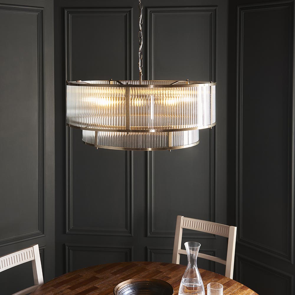 Endon Rothbury 8 light tiered chandelier in antique brass with clear ribbed glass panels, suspended from a chain in a dark panelled dining room.