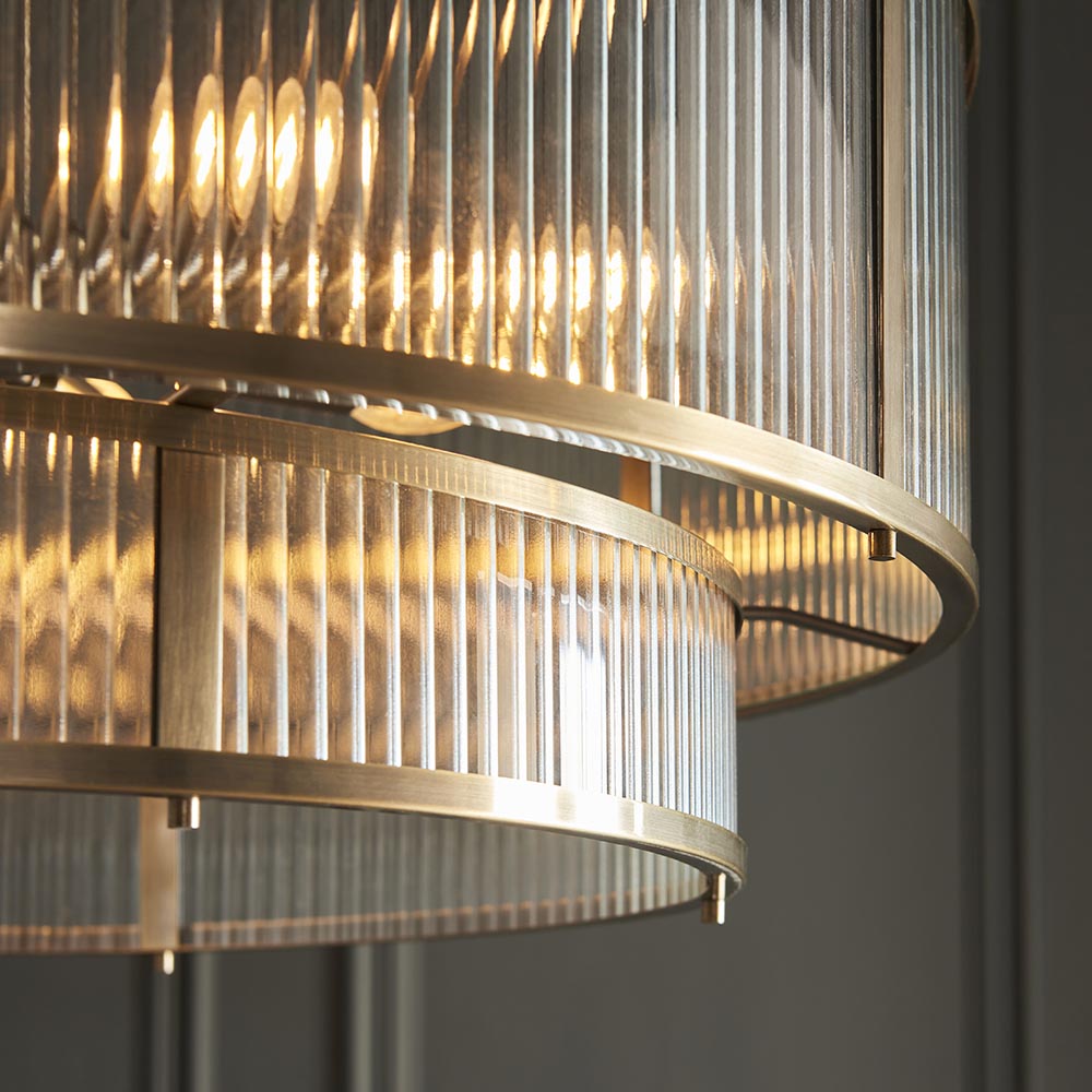 Close-up of Endon Rothbury 8 Light Tiered Chandelier in antique brass, showing the two ribbed clear glass tiers and warm-lit lamps within the brass frame.
