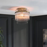 Endon Beaumont flush ceiling light in antique brass with tiered glass rod shade, illuminated on a white ceiling above dark panelled walls.