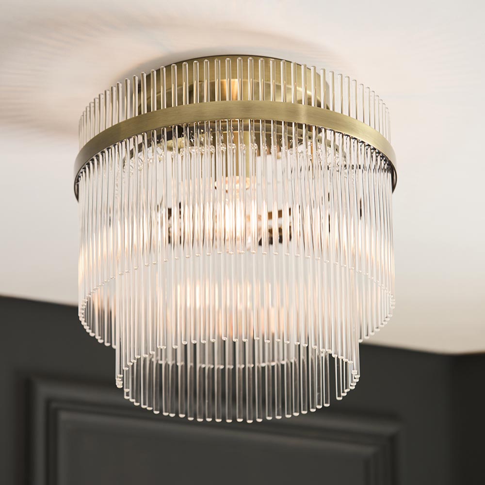Endon Beaumont flush ceiling light in antique brass, with tiered glass rod shade mounted against a white ceiling above a dark panelled wall.
