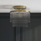 Endon Beaumont flush ceiling light in antique brass, with a two-tier glass rod shade mounted against a white ceiling above a dark panelled wall.