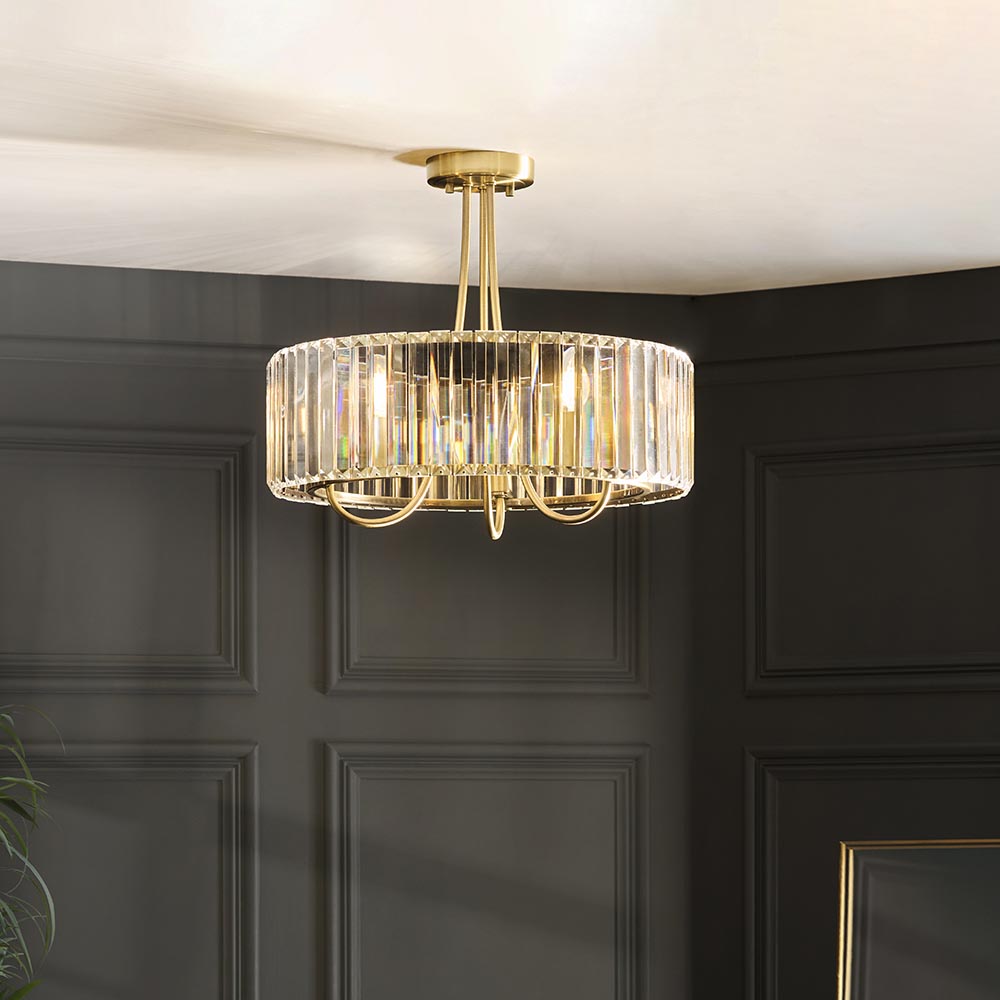 Fairfax 3-light semi-flush ceiling light in antique brass, round crystal glass shade with looping brass arms, shown mounted in a dark panelled room.