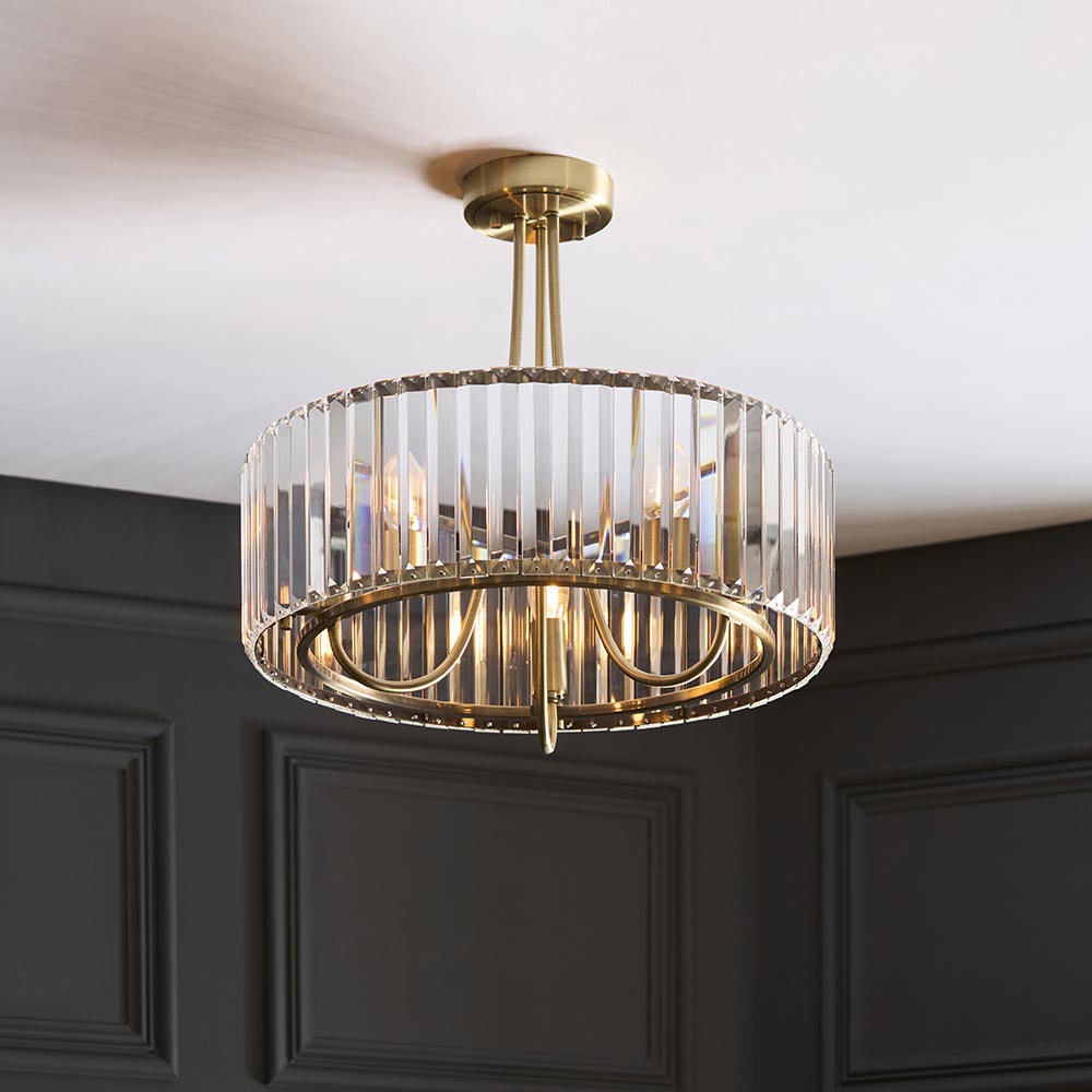 Fairfax 3-light semi-flush ceiling light in antique brass with vertical crystal glass panels, shown mounted in a room with dark panelled walls.