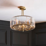 Fairfax 3-light semi-flush ceiling light in antique brass with vertical crystal glass panels, shown mounted in a room with dark panelled walls.