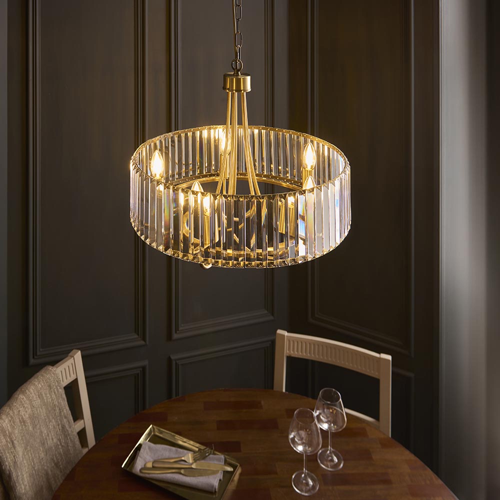Fairfax 5 Light Pendant in antique brass with faceted crystal glass panels, hung above a wooden dining table in a dark panelled room.