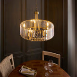 Fairfax 5 Light Pendant in antique brass with faceted crystal glass panels, hung above a wooden dining table in a dark panelled room.