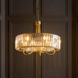 Fairfax 5 Light Pendant in antique brass, round drum frame with faceted crystal glass panels, hung from a chain on dark wood panelled wall.